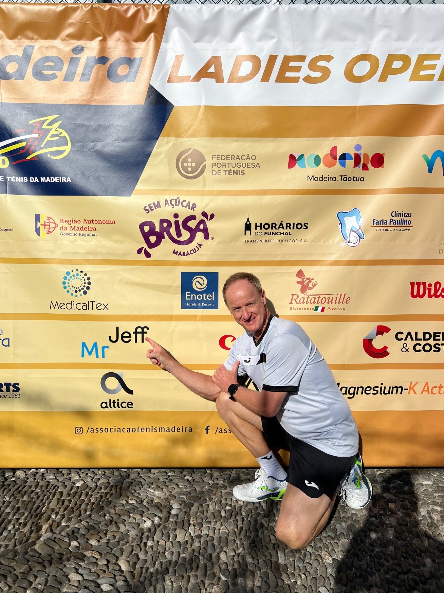 Jeff King smiling and pointing at his name on the Madeira Ladies Open sponsor board.